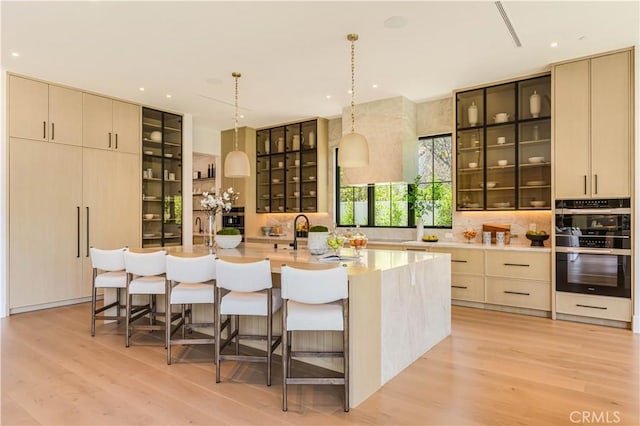 16711 Moorpark St, Encino, CA 91436 - kitchen featuring decorative backsplash, a center island with sink, light wood-style flooring, glass insert cabinets, and a kitchen bar