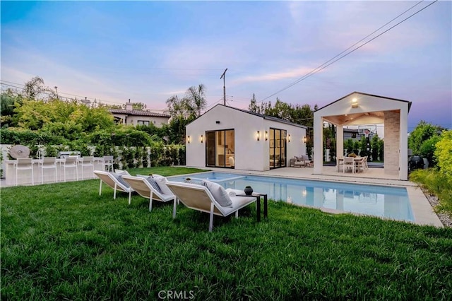 16711 Moorpark St, Encino, CA 91436 - back of house at dusk featuring an outdoor structure, a lawn, an outdoor pool, a storage structure, and a patio area