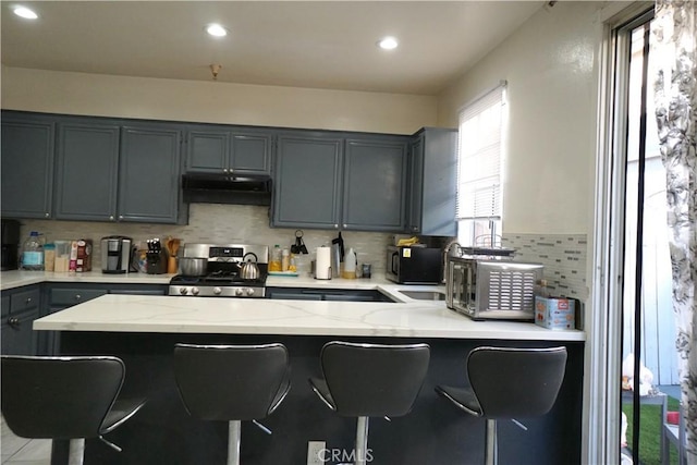 18347 Saticoy St Unit 33, Reseda, CA 91335 - kitchen with stainless steel stove, under cabinet range hood, light stone countertops, decorative backsplash, and gray cabinetry