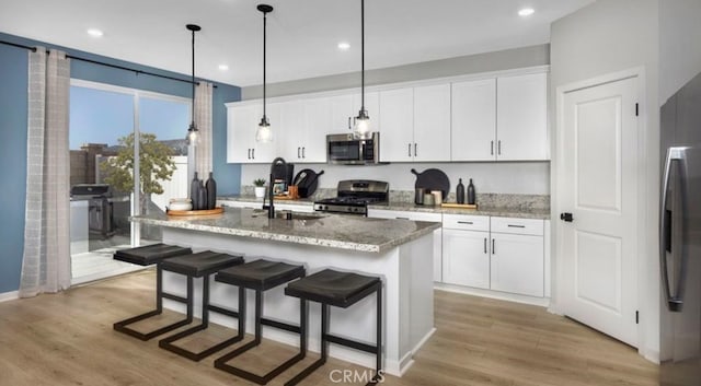 32739 Crystal Cove Ct, Winchester, CA 92596 - kitchen featuring appliances with stainless steel finishes, light wood-type flooring, white cabinetry, decorative light fixtures, and a kitchen island with sink