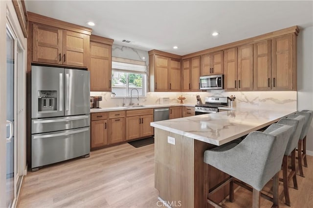 9180 Araujo Ct, Atascadero, CA 93422 - kitchen with stainless steel appliances, a peninsula, light stone counters, light wood-style flooring, and recessed lighting