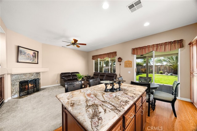 14067 Glendale Ct, Rancho Cucamonga, CA 91739 - kitchen with a ceiling fan, light stone counters, brown cabinetry, a fireplace, and a center island