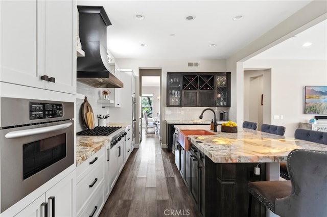 982 Camino Del Arroyo Dr Unit 49, San Marcos, CA 92078 - kitchen with wall chimney exhaust hood, a breakfast bar area, backsplash, dark wood-type flooring, and light stone countertops