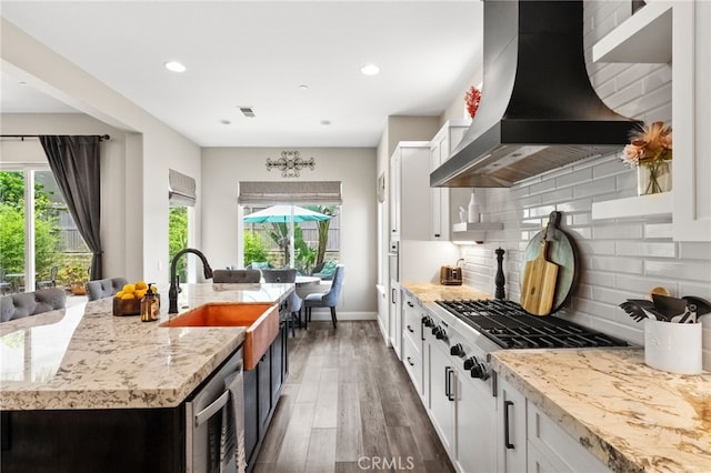 982 Camino Del Arroyo Dr Unit 49, San Marcos, CA 92078 - kitchen featuring wall chimney exhaust hood, stainless steel gas stovetop, wood finished floors, white cabinetry, and an island with sink