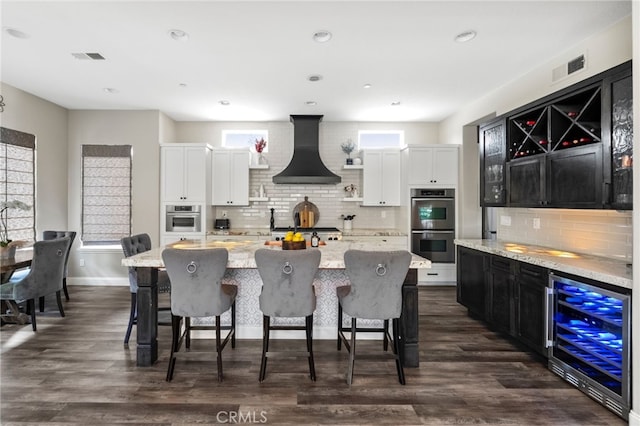 982 Camino Del Arroyo Dr Unit 49, San Marcos, CA 92078 - kitchen with beverage cooler, wall chimney exhaust hood, stainless steel double oven, decorative backsplash, and light stone counters