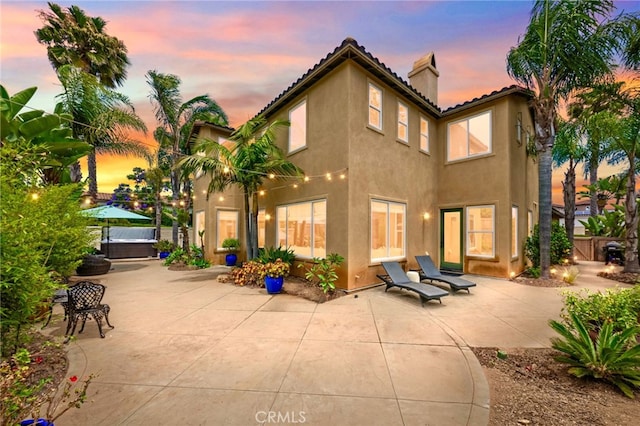 982 Camino Del Arroyo Dr Unit 49, San Marcos, CA 92078 - back of property at dusk with a patio, a chimney, stucco siding, and a hot tub