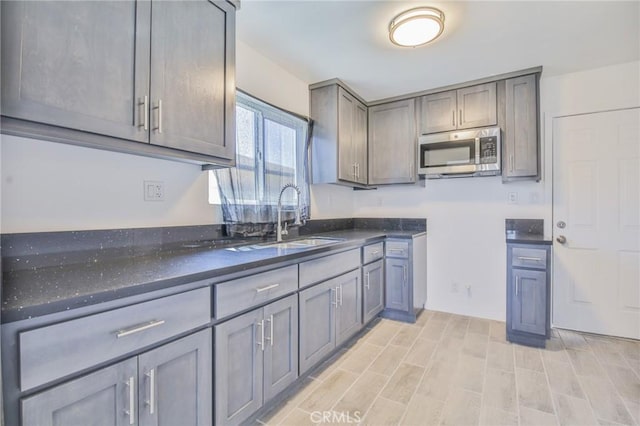 1026 W 109th St, Los Angeles, CA 90044 - kitchen featuring stainless steel microwave, gray cabinetry, dark stone counters, and light wood finished floors