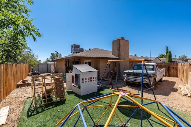 1267 Joshua Tree Dr, Barstow, CA 92311 - back of house featuring a storage unit, a chimney, a fenced backyard, a playground, and a shingled roof