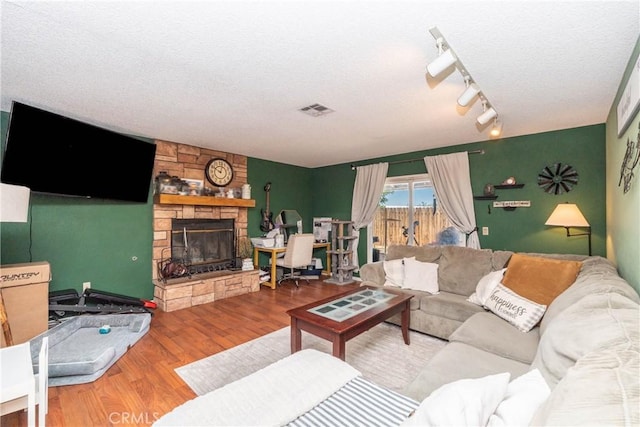 1267 Joshua Tree Dr, Barstow, CA 92311 - living room featuring wood finished floors, a stone fireplace, a textured ceiling, and rail lighting