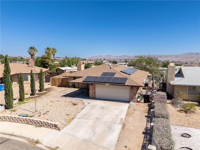 1267 Joshua Tree Dr, Barstow, CA 92311 - view of front of home featuring an attached garage, roof mounted solar panels, driveway, stone siding, and a mountain view
