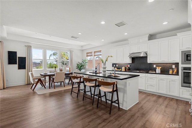 19162 Lauren Ln, Saugus, CA 91350 - kitchen with appliances with stainless steel finishes, dark countertops, under cabinet range hood, wood finished floors, and recessed lighting