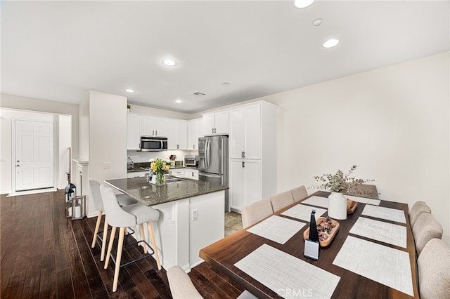 8495 E Preserve Loop, Chino, CA 91708 - kitchen with appliances with stainless steel finishes, a kitchen bar, a center island with sink, white cabinetry, and dark wood-type flooring