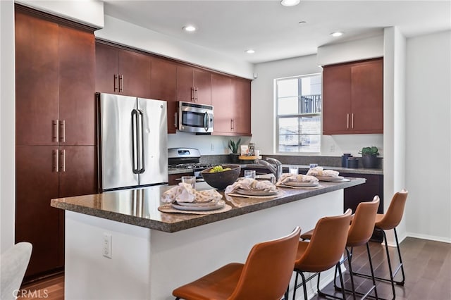 2950 19th St Unit 113, Signal Hill, CA 92707 - kitchen featuring appliances with stainless steel finishes, a breakfast bar area, dark wood finished floors, recessed lighting, and a center island with sink