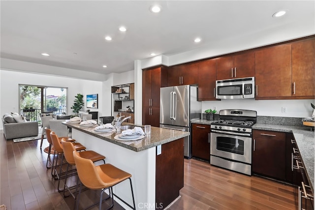 2950 19th St Unit 113, Signal Hill, CA 92707 - kitchen with appliances with stainless steel finishes, open floor plan, dark wood-type flooring, a kitchen bar, and dark stone counters