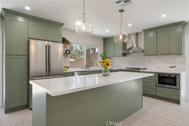 22 Sage Cyn, Pomona, CA 91766 - kitchen with green cabinetry, wall chimney exhaust hood, decorative backsplash, appliances with stainless steel finishes, and hanging light fixtures