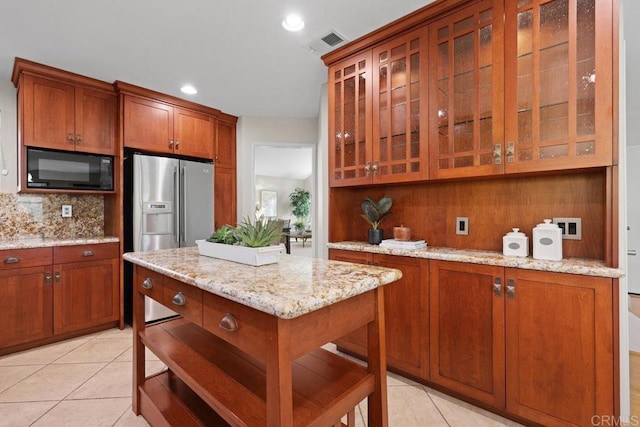 9481 Deanly St, Lakeside, CA 92040 - kitchen with black microwave, stainless steel refrigerator with ice dispenser, light tile patterned flooring, brown cabinets, and light stone counters