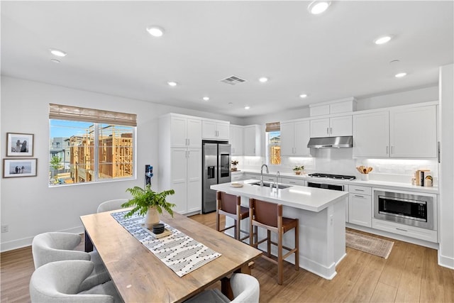 1281 Windmill Rd, Rancho Mission Viejo, CA 92694 - kitchen with under cabinet range hood, stainless steel appliances, an island with sink, white cabinets, and a kitchen breakfast bar