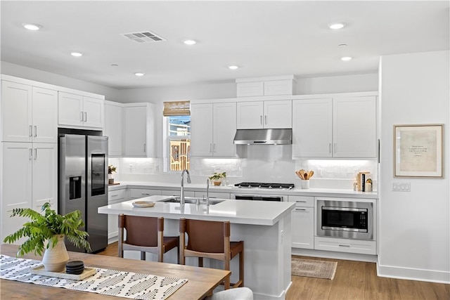 1281 Windmill Rd, Rancho Mission Viejo, CA 92694 - kitchen with appliances with stainless steel finishes, under cabinet range hood, light countertops, light wood-style floors, and a center island with sink