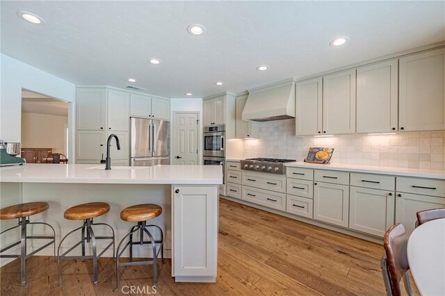 770 Warbler Ct, Merced, CA 95340 - kitchen featuring custom range hood, stainless steel appliances, a breakfast bar, decorative backsplash, and light countertops