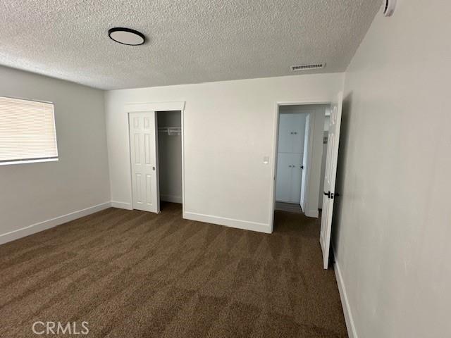 211-215 E California Ave, Ridgecrest, CA 93555 - unfurnished bedroom featuring a textured ceiling, dark carpet, and a closet