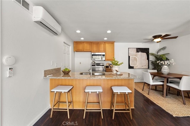 21981 Rimhurst Dr Unit 158, Lake Forest, CA 92630 - kitchen featuring appliances with stainless steel finishes, a wall mounted AC, a peninsula, light stone counters, and a breakfast bar