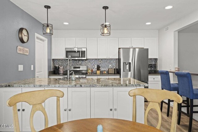 3151 W Hemlock St, Oxnard, CA 93035 - kitchen with appliances with stainless steel finishes, backsplash, light stone counters, white cabinetry, and pendant lighting
