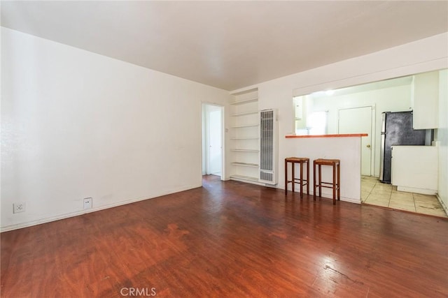 1132 E 65th St, Los Angeles, CA 90001 - unfurnished living room featuring a heating unit, light wood finished floors, and built in shelves