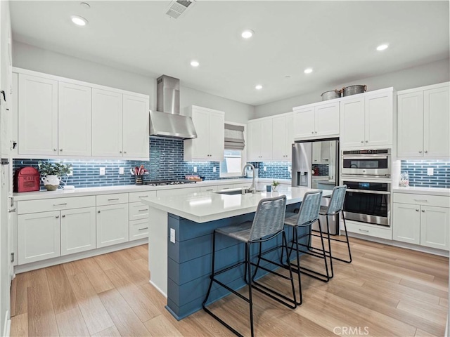 27717 Knoll View Pl, Valencia, CA 91381 - kitchen with wall chimney exhaust hood, decorative backsplash, appliances with stainless steel finishes, a kitchen bar, and light wood-style flooring