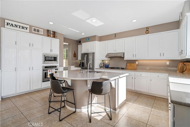 43145 62nd St W, Lancaster, CA 93536 - kitchen with stainless steel appliances, under cabinet range hood, white cabinets, a center island with sink, and light tile patterned floors