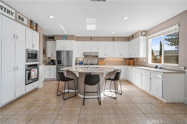 43145 62nd St W, Lancaster, CA 93536 - kitchen featuring stainless steel appliances, under cabinet range hood, a breakfast bar area, light tile patterned floors, and white cabinets
