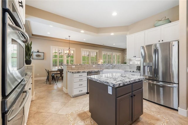 79787 Parkway Esplanade N, La Quinta, CA 92253 - kitchen featuring appliances with stainless steel finishes, a peninsula, white cabinets, tasteful backsplash, and light stone countertops
