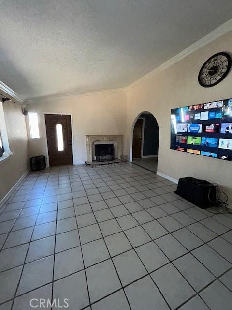 18145 10th St, Bloomington, CA 92316 - unfurnished living room featuring crown molding, a textured ceiling, light tile patterned floors, a fireplace with raised hearth, and arched walkways