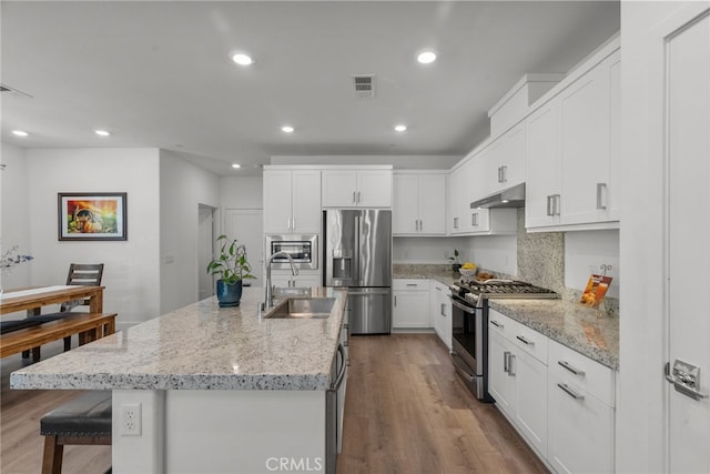 12062 Turnleaf Ave, Whittier, CA 90602 - kitchen with appliances with stainless steel finishes, under cabinet range hood, dark wood-style flooring, white cabinetry, and a kitchen breakfast bar