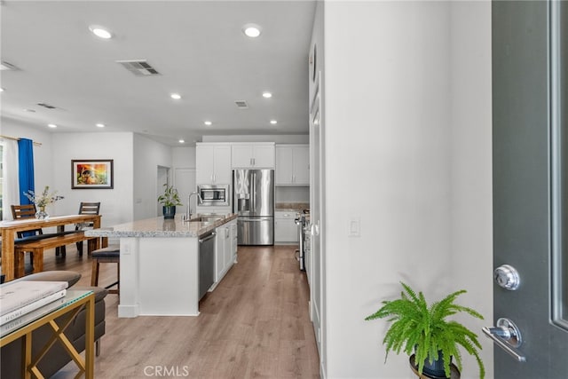 12062 Turnleaf Ave, Whittier, CA 90602 - kitchen with appliances with stainless steel finishes, white cabinetry, light wood finished floors, light stone counters, and an island with sink