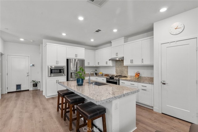 12062 Turnleaf Ave, Whittier, CA 90602 - kitchen featuring appliances with stainless steel finishes, under cabinet range hood, light wood finished floors, a center island with sink, and light stone counters