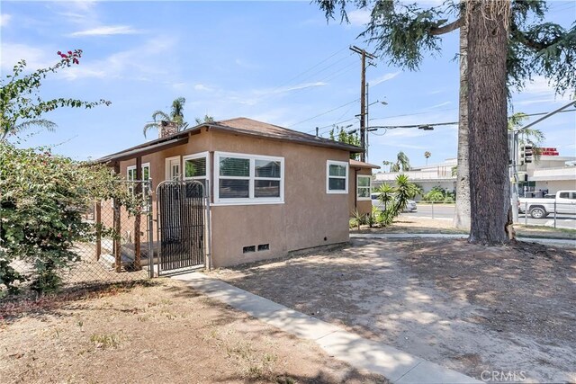6017 Brockton Ave, Riverside, CA 92506 - view of side of home with a gate, stucco siding, and a chimney