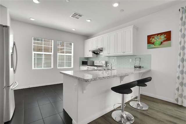 8595 Founders Grove St, Chino, CA 91708 - kitchen featuring under cabinet range hood, freestanding refrigerator, a peninsula, white cabinetry, and stove
