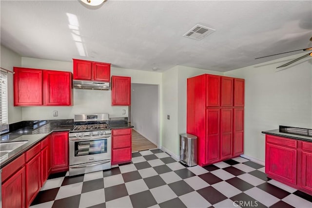 2917 Fairfield Ave, Palmdale, CA 93550 - kitchen with stainless steel gas range, under cabinet range hood, reddish brown cabinets, dark flooring, and dark countertops