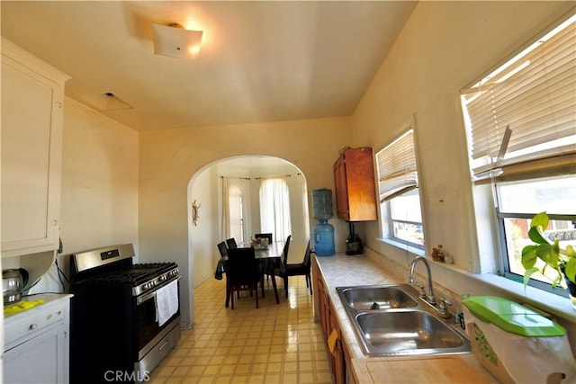 3945 Woolwine Dr, Los Angeles, CA 90063 - kitchen featuring stainless steel range with gas cooktop, arched walkways, light countertops, light floors, and white cabinetry