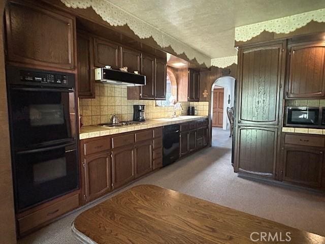 1220 W L St, Wilmington, CA 90744 - kitchen with black appliances, tile counters, arched walkways, light colored carpet, and decorative backsplash