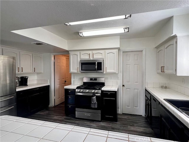 14016 Las Entradas, Bakersfield, CA 93314 - kitchen with appliances with stainless steel finishes, tile counters, dark wood finished floors, white cabinets, and a textured ceiling