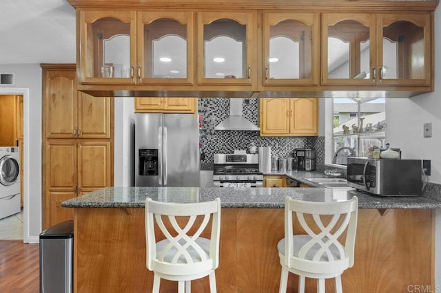 2164 Bluehaven Ct, San Diego, CA 92154 - kitchen featuring stainless steel appliances, wall chimney range hood, dark stone counters, washer / clothes dryer, and a peninsula