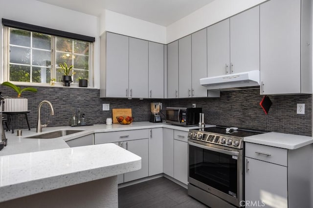 17 Carnegie, San Jose, CA 95116 - kitchen with stainless steel range with electric cooktop, under cabinet range hood, decorative backsplash, light stone counters, and gray cabinetry