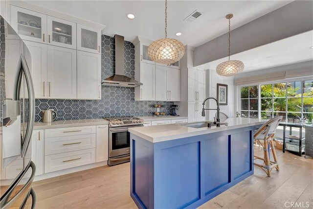 19325 Peachtree Ln, Huntington Beach, CA 92648 - kitchen featuring stainless steel appliances, wall chimney exhaust hood, light wood-style flooring, light countertops, and a center island with sink