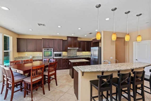 16858 Mariposa Ave, Riverside, CA 92504 - kitchen with appliances with stainless steel finishes, a kitchen island with sink, dark brown cabinets, decorative backsplash, and light tile patterned floors