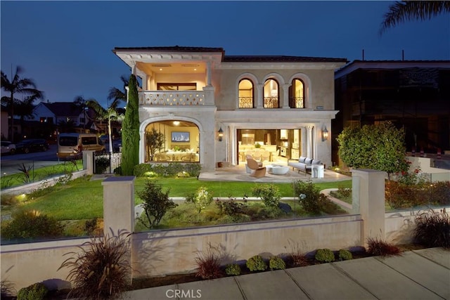 3300 Ocean Blvd, Corona Del Mar, CA 92625 - back of house at twilight with a balcony, a fenced front yard, stucco siding, and outdoor lounge area