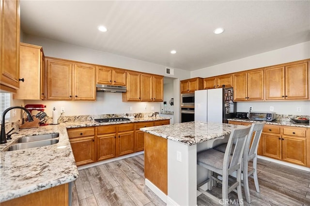 33883 Vinca Ln, Murrieta, CA 92563 - kitchen featuring appliances with stainless steel finishes, under cabinet range hood, light wood-type flooring, a center island, and light stone countertops