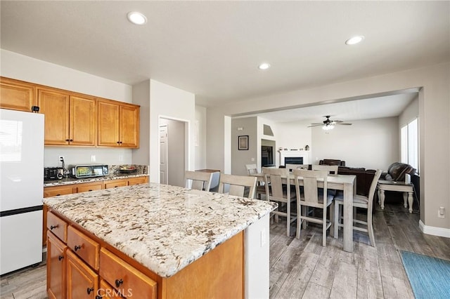 33883 Vinca Ln, Murrieta, CA 92563 - kitchen with freestanding refrigerator, ceiling fan, light wood finished floors, light stone counters, and open floor plan