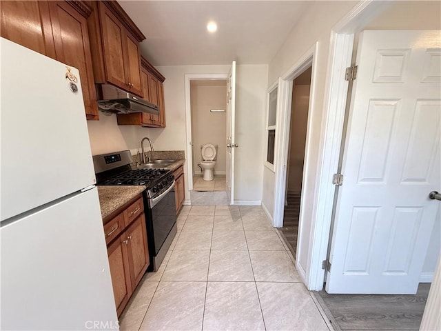 4449 Walnut St, Baldwin Park, CA 91706 - kitchen featuring freestanding refrigerator, under cabinet range hood, stainless steel gas stove, brown cabinetry, and light tile patterned floors