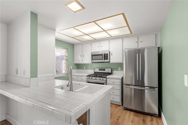 6355 Ortega St, Chino, CA 91710 - kitchen featuring appliances with stainless steel finishes, tile counters, a peninsula, white cabinetry, and light wood-style floors
